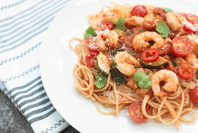 A plate of prawn, chilli and tomato spaghetti garnished with coriander and cheese