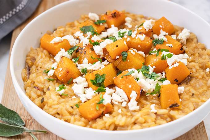 A white bowl containing roasted butternut squash risotto, topped with crumbled feta cheese and fresh sage.
