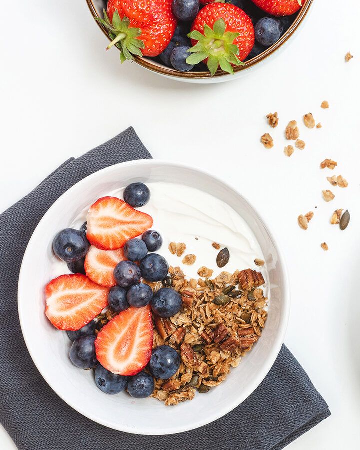 A white bowl containing granola, yoghurt, strawberries and blueberries