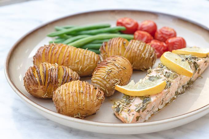 A plate containing roasted salmon and hasselback potatoes, green beans and tomatoes