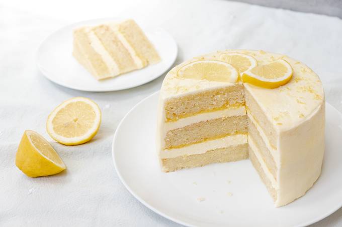 A lemon layer cake on a white plate, sliced open to reveal lemon curd and lemon icing in the centre