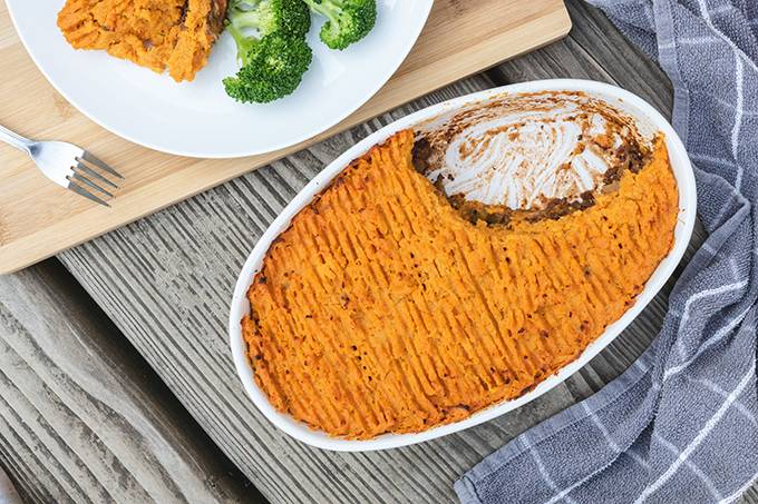 Top down view of a large oven dish containing sweet potato cottage pie, with one portion on a white plate next to it