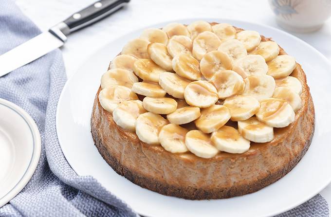 A banoffee cheesecake on a white plate, topped with sliced bananas and caramel sauce