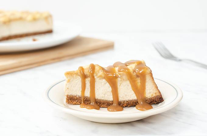 A slice of banoffee cheesecake drizzled with caramel sauce on a white plate