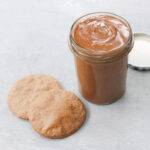 An open jar containing homemade gluten-free Biscoff spread and two Biscoff biscuits