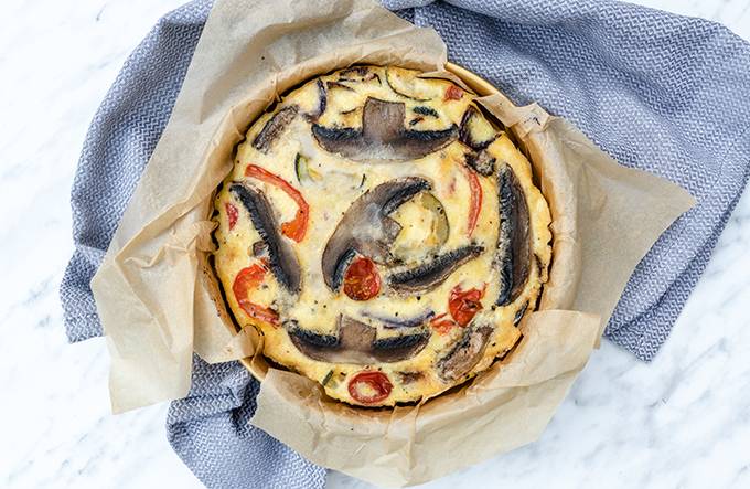 Top down view of a tin of roasted vegetable frittata, with baking paper around the edges.