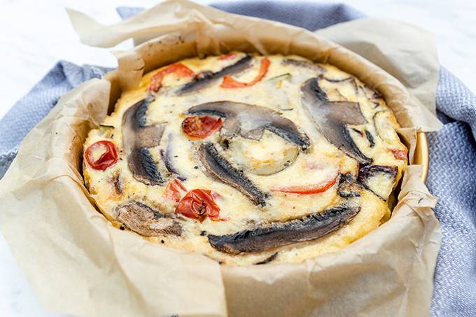 Close up of a roasted vegetable frittata in a tin with baking paper around the edges.