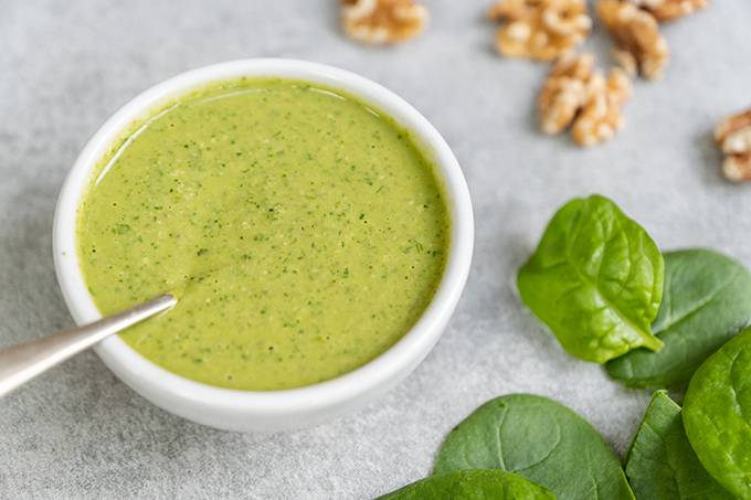 A small white bowl filled with pesto sauce and a silver spoon resting in it.