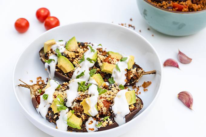 A bowl containing two halves of a stuffed aubergine, topped with avocado and yoghurt