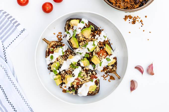 A bowl containing two halves of a stuffed aubergine, topped with avocado and yoghurt