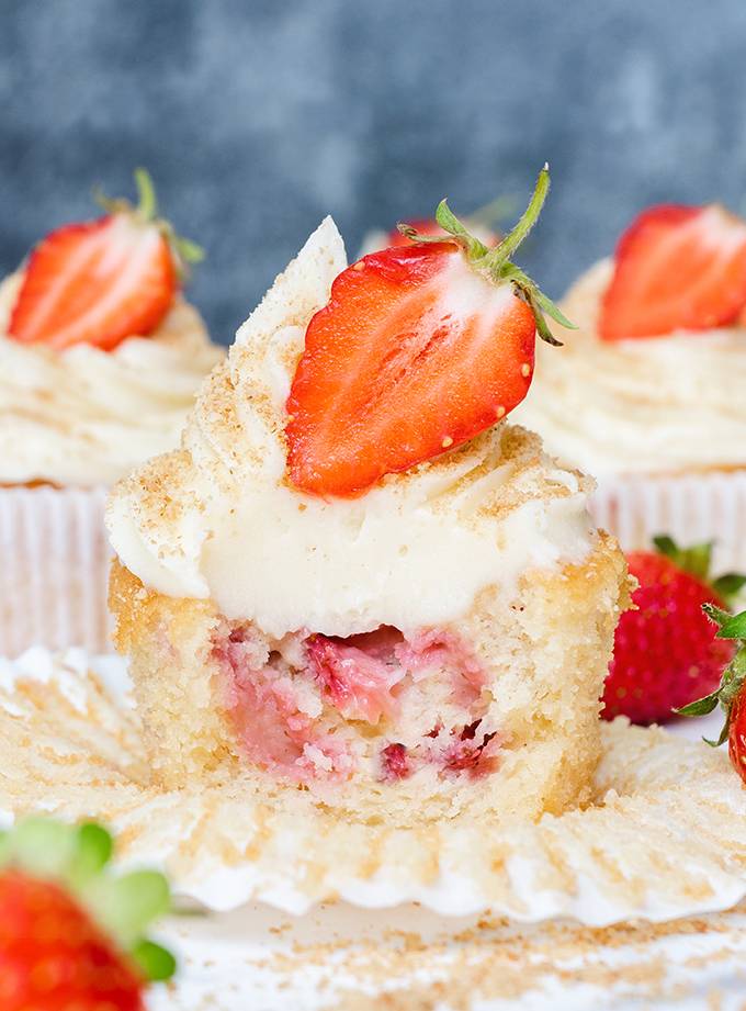 Close up of a white chocolate and strawberry cheesecake cupcake, cut open to reveal baked strawberry pieces in the middle.