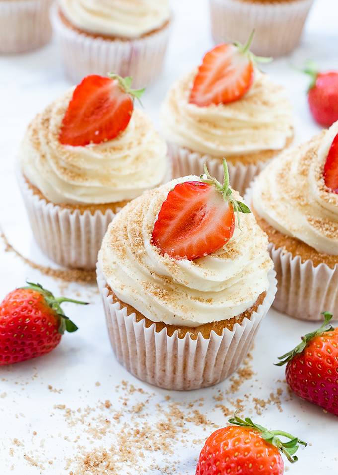 Four cupcakes decorated with white chocolate and cream cheese icing swirls and half a strawberry.