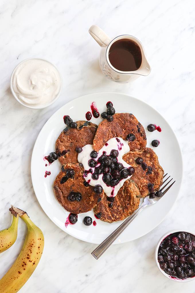 Top down view of a plate of banana bread pancakes, topped with yoghurt and blueberries.