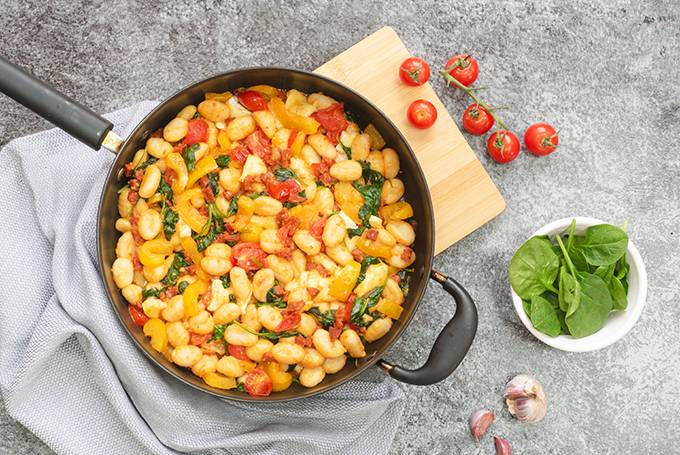 Top down view of a pan containing gnocchi cooked with vegetables, chorizo and brie