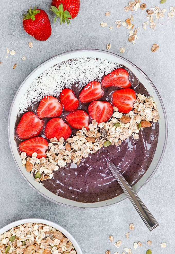 Top down view of a purple smoothie bowl with strawberries, coconut flakes and granola on top.