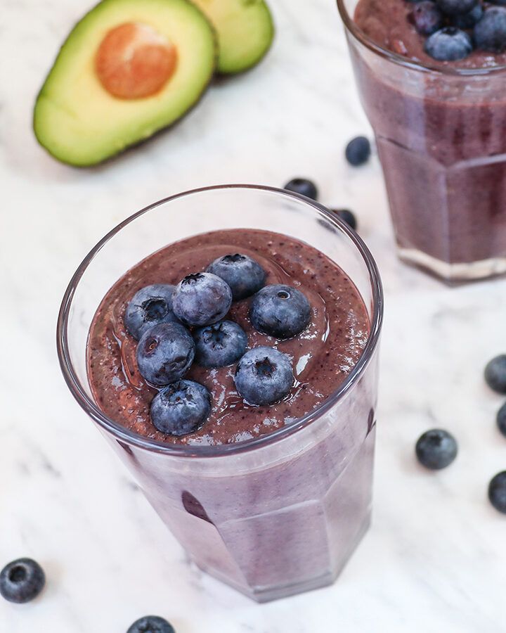 A glass of blueberry avocado smoothie with fresh blueberries on top.