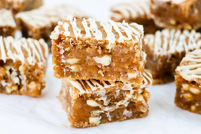 Two peanut butter blondies stacked on top of each other, surrounded by other blondies. Each is drizzled with white chocolate.
