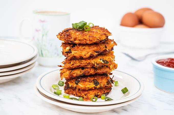 A stack of crispy sweet potato hash browns on a plate, sprinkled with spring onion slices.