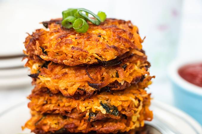 Close up of a stack of crispy sweet potato hash browns with some spring onion slices on top.