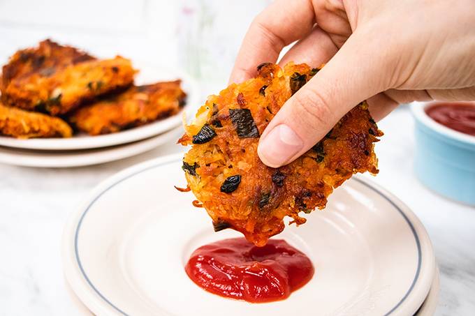 A crispy sweet potato hash brown being dipped in some tomato ketchup on a plate.