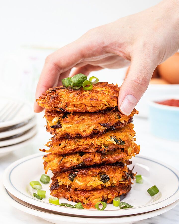 A stack of crispy sweet potato hash browns on a plate, sprinkled with spring onion slices.