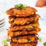 A stack of crispy sweet potato hash browns on a plate, sprinkled with some slices of spring onion.