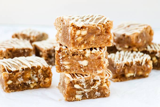 Three peanut butter blondies stacked on top of each other, surrounded by other blondies. Each is drizzled with white chocolate.