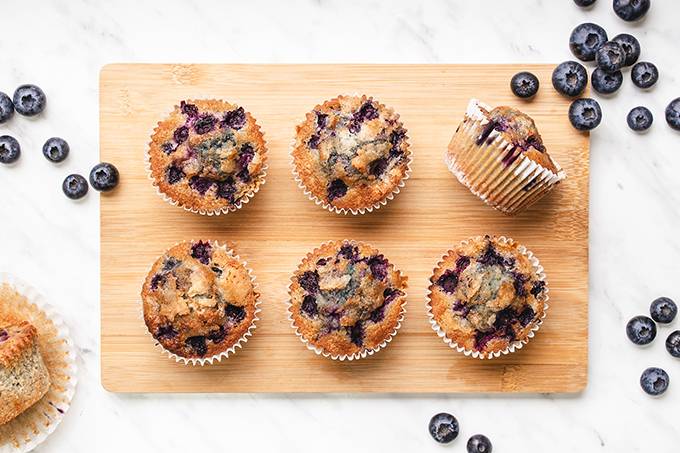 Top down view of some gluten free blueberry muffins on a wooden board, surrounded by some clusters of fresh blueberries.