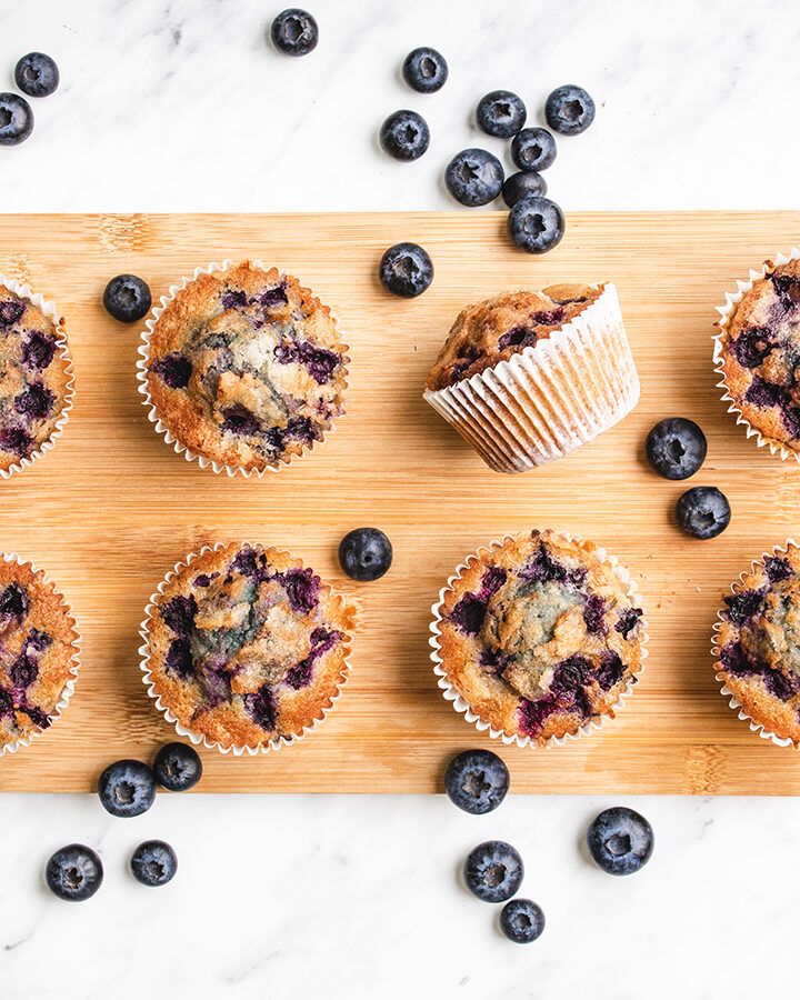 Top down view of some gluten free blueberry muffins on a wooden board, surrounded by some clusters of fresh blueberries.