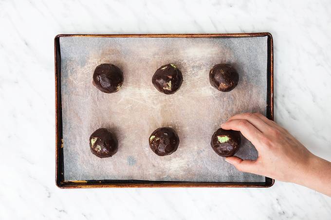 Top down view of a baking tray containing six balls of aero mint chocolate chip cookie dough balls ready to be baked.