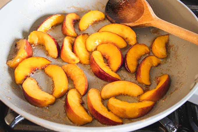 Peach slices caramelising in a saucepan with a wooden spoon resting in it