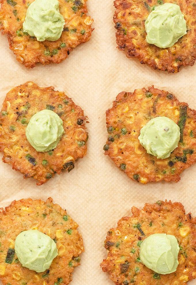 Six vegetable fritters laid out on baking paper, each with a dollop of guacamole in the centre.