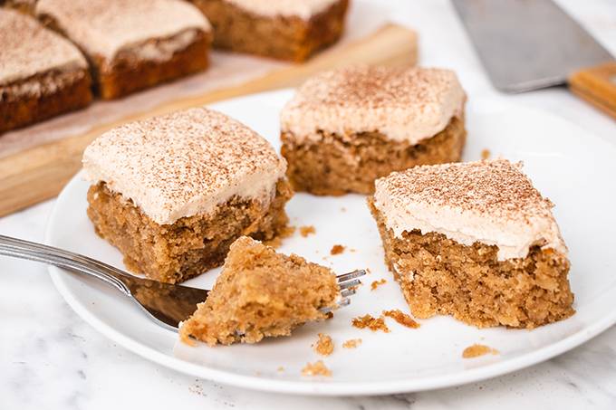 Three squares of apple and cinnamon cake on a white plate, one with a forkful cut away from it.