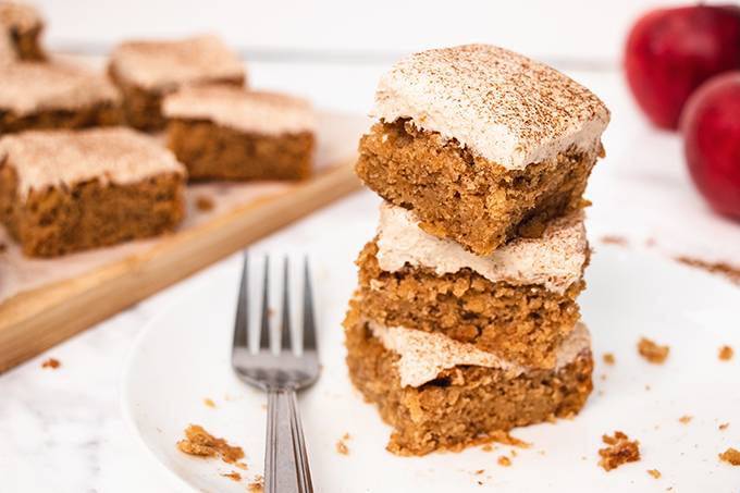 A stack of three squares of apple and cinnamon cake on a white plate with a silver fork next to it.