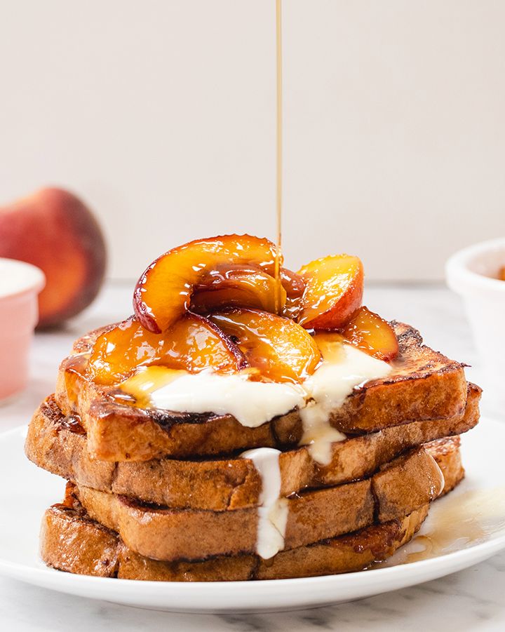 A plate of French toast topped with caramelised peaches and yoghurt, being drizzled with maple syrup