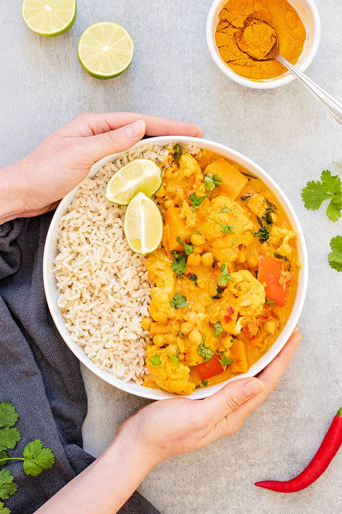 Top down view of a bowl of cauliflower and chickpea curry held in a person's hands