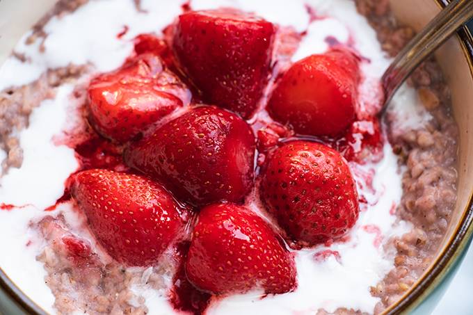 Close up of a bowl of porridge topped with coconut cream and cooked strawberries