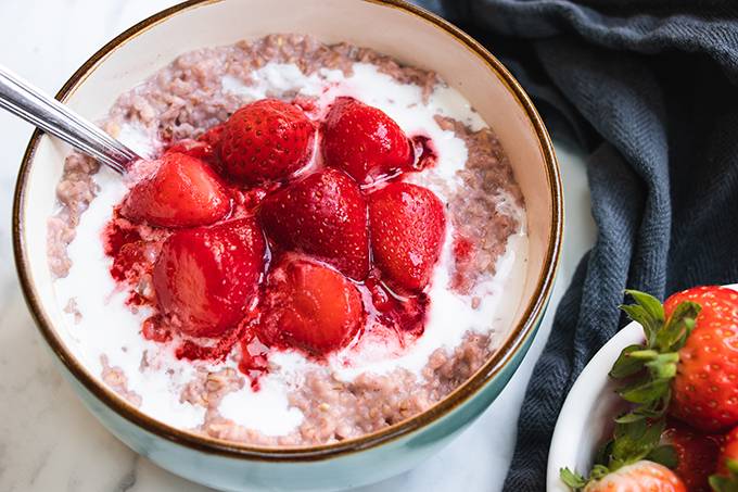 A bowl of porridge topped with coconut cream and cooked strawberries