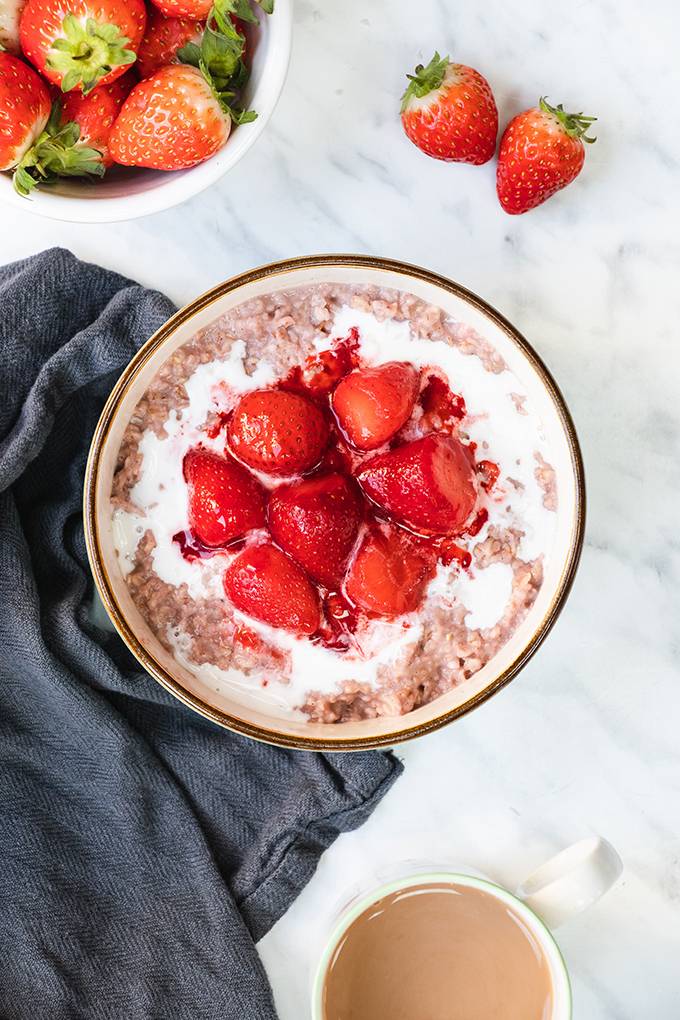 Top down view of a bowl of porridge topped with coconut cream and cooked strawberries