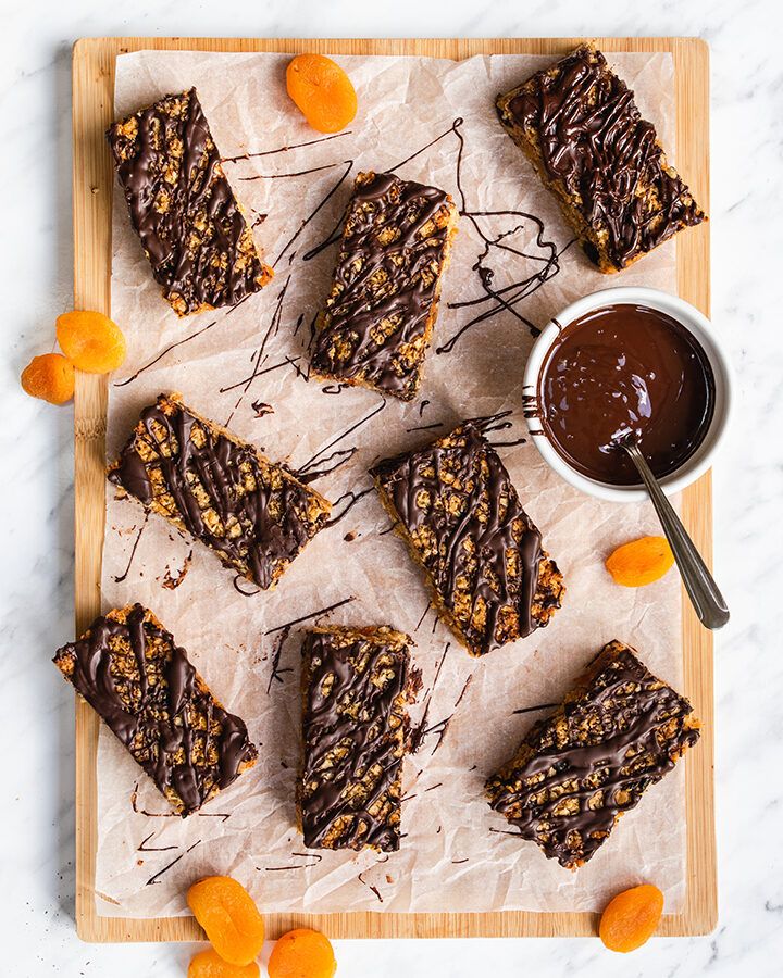 Top down view of chocolate apricot flapjacks on a wooden board, and a pot of melted dark chocolate.