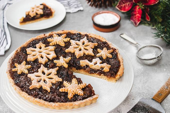 A Christmas mincemeat tart, with one slice cut out of it and put on a plate in the background.
