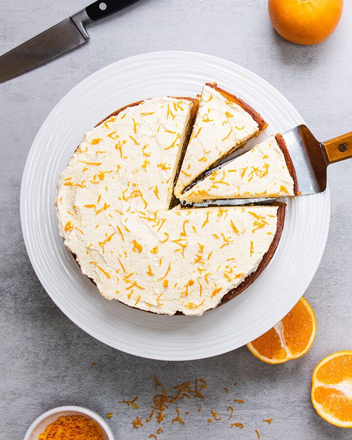 Top down view of an orange and almond cake with icing and orange zest on top,
