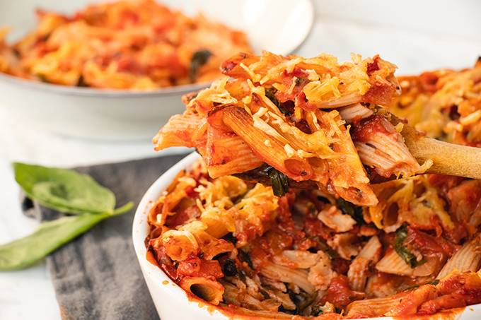 Close up of a dairy free cheese and tomato pasta bake with spoonful being taken out of the dish.