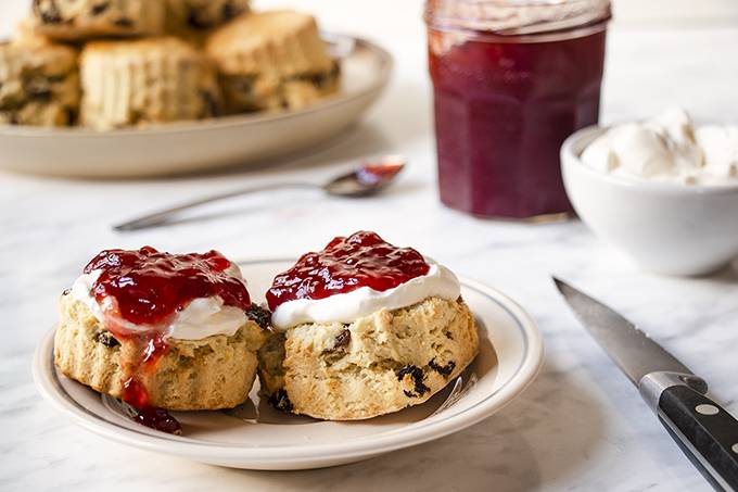 A scone on a white plate, cut in half and topped with cream and jam.