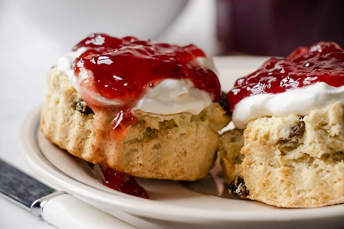 Close up of a gluten and dairy free scone topped with cream and jam.