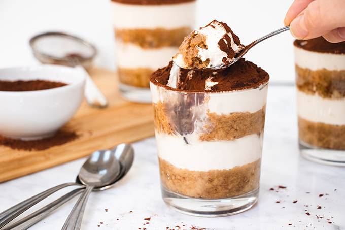 A glass pot of layered gluten and dairy free tiramisu dessert, with a spoonful taken out of it