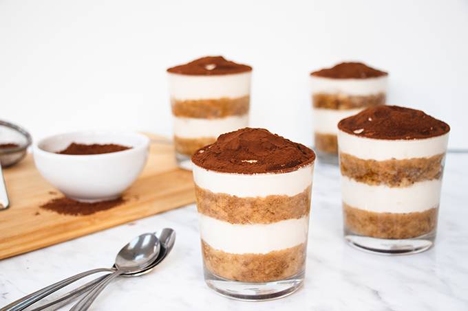 Four single portion pots of layered gluten and dairy free tiramisu, each dusted with cocoa powder
