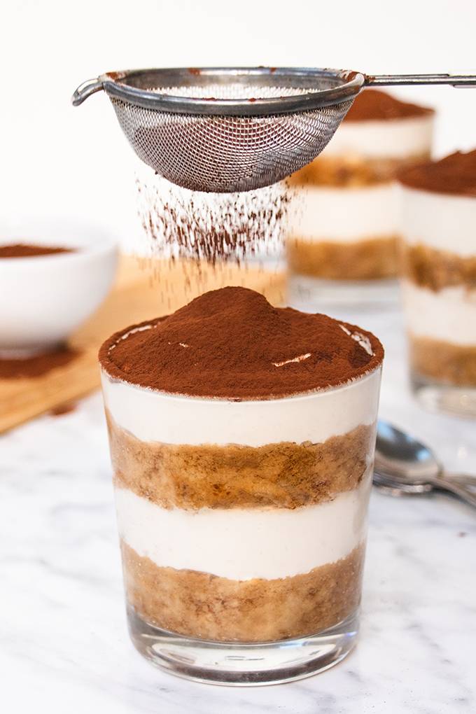 A pot of gluten and dairy free tiramisu being sprinkled with cocoa powder from a sieve