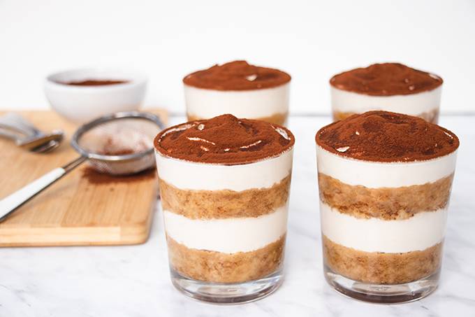 Four single portion pots of layered gluten and dairy free tiramisu, each dusted with cocoa powder