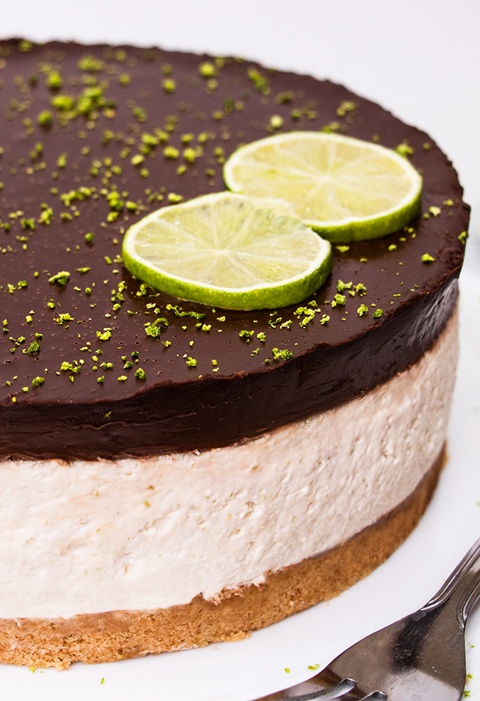 Close up of a dairy free lime cheesecake with a chocolate ganache topping and two lime slices as decoration.